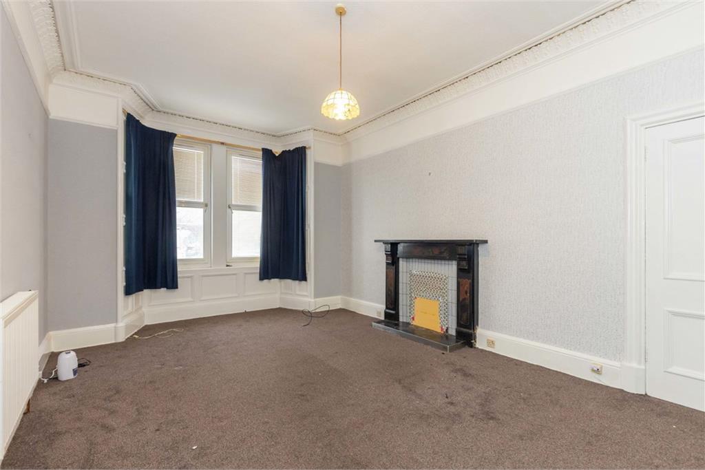 An empty living room with light grey walls, brow carpet and navy curtains. There's a dark fireplace on the right hand side.