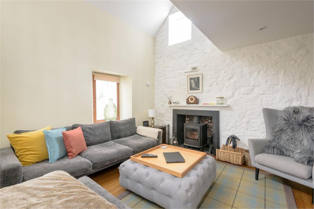 A spacious and wlel-lit living room with grey sofa, old fashioned fireplace, and tartan rug.