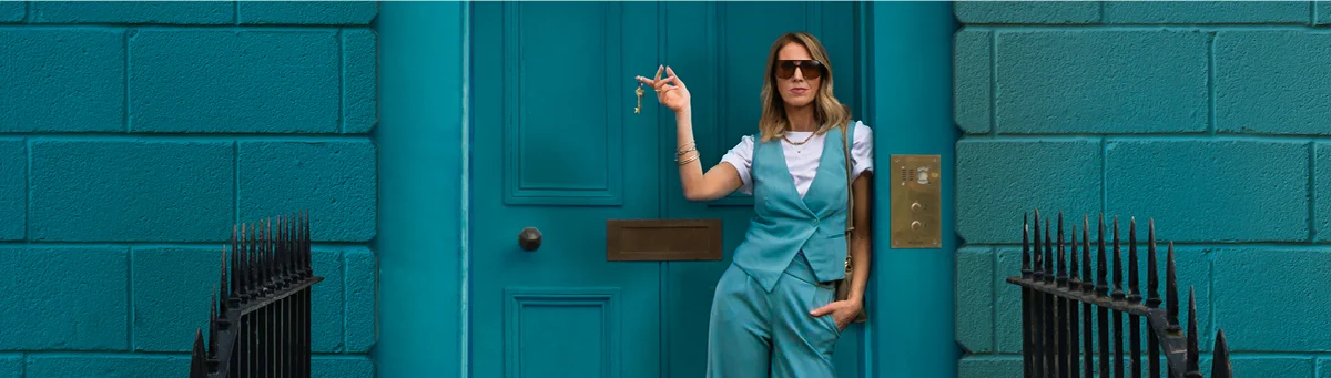 A woman wearing sunglasses stands in front of a blue door, holding keys in her right hand